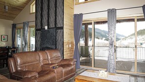 Een gezellige woonkamer met een leren bank, een houten salontafel en een grote schuifdeur die uitkomt op een balkon met uitzicht op de bergen.