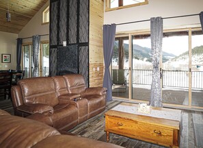 A cozy living room with a leather sofa, a wooden coffee table, and a large sliding glass door leading to a balcony with a mountain view. - A remote private mountain retreat complete with a 4WD 4 seat side by side (Bridger)