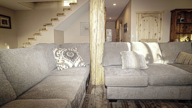 A living room with two grey sofas, a wooden pillar, a staircase, and a wooden cabinet.