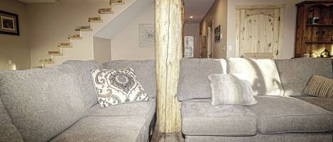 A living room with two grey sofas, a wooden pillar, a staircase, and a wooden cabinet.