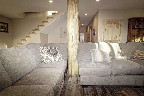 A living room with two grey sofas, a wooden pillar, a staircase, and a wooden cabinet.