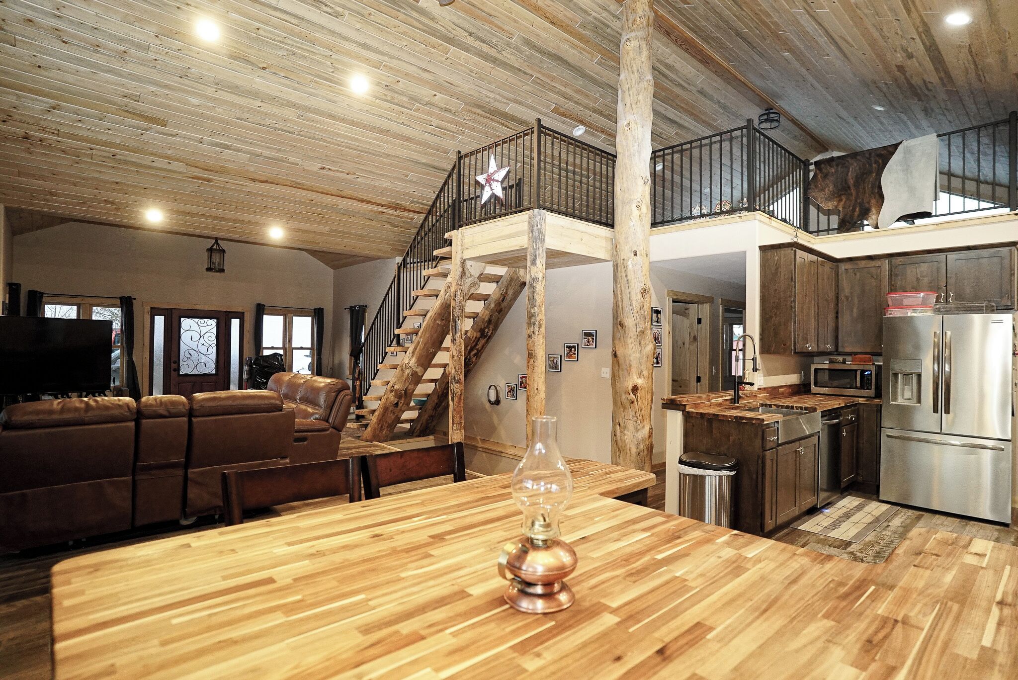 A spacious living area with a wooden floor, a staircase, a kitchen with modern appliances, and a large window.