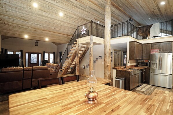 A spacious living area with a wooden floor, a staircase, a kitchen with modern appliances, and a large window.