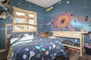 A bedroom with a bed, a desk, and a wall mural.