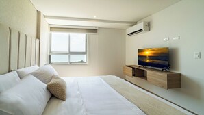 Ein modernes Hotelzimmer mit einem großen Bett, einem flachbildfernseher an einer Holzkassette, einem Fenster mit Blick auf den Himmel und einer Klimaanlage an der Wand.