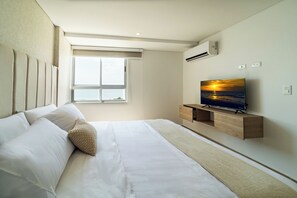 A modern hotel room with a large bed, a flat-screen TV mounted on a wooden console, a window with a view of the sky, and an air conditioning unit on the wall. - Oceani Towers Cielo Mar · Rooftop, beach 5 min (Cartagena de Indias)