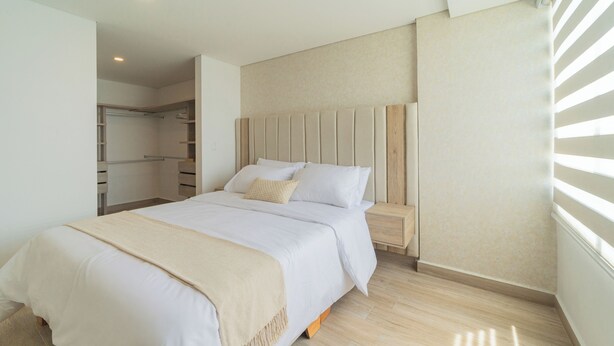 Ein Schlafzimmer mit einem Bett, einem Holzkopfteil, einem Nachttisch und einem begehbaren Kleiderschrank.