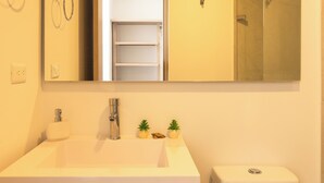 Ein Badezimmer mit einem weißen Waschbecken, einem Spiegel und einer Toilette. Auf der Ablage über dem Waschbecken stehen zwei kleine Topfpflanzen.