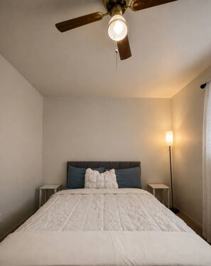 A bedroom with a bed, a ceiling fan, bedside tables, and a floor lamp. - Bright & Comfortable Retreat - 2BR Apartment (Waxahachie)