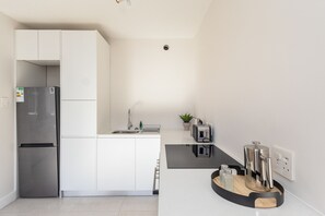 Eine moderne Küche mit einem Edelstahl-Kühlschrank, weißen Schränken, einer schwarzen Arbeitsplatte und einer integrierten Spüle.
