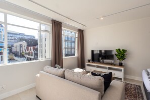 A modern living room with a sofa, TV, and a view of buildings through large windows. - Bright City Studio in the Heart of Cape Town (Cape Town)