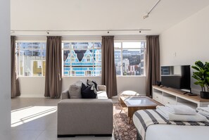 A modern living room with a sofa, a coffee table, a TV, and a large window with curtains. - Bright City Studio in the Heart of Cape Town (Cape Town)