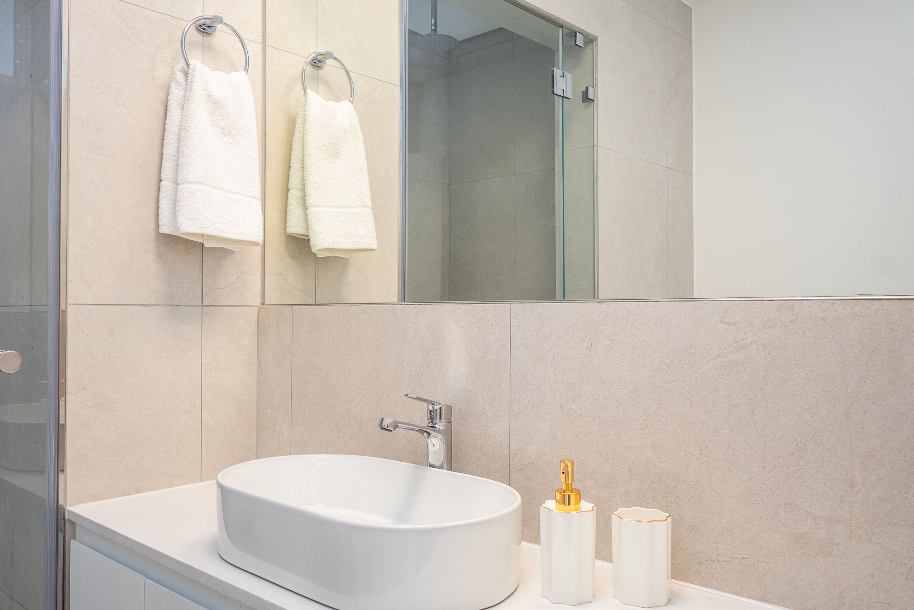 A modern bathroom with a large mirror, a white sink, and two towels hanging on a towel rack.