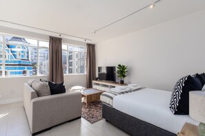 Ein modernes Hotelzimmer mit einem großen Bett, einem Sofa, einem Fernseher und Blick auf umliegende Gebäude.