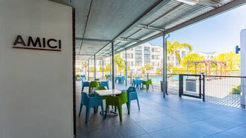Un patio al aire libre con mesas y sillas, un cartel que dice "AMICI" y una vista de edificios y árboles al fondo.
