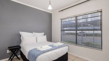 Un dormitorio con una cama, una mesita de noche, una lámpara colgante y una ventana con persianas.