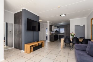 Uma sala de estar moderna com uma televisão de tela plana, um banco de madeira e uma área de jantar com mesa e cadeiras.