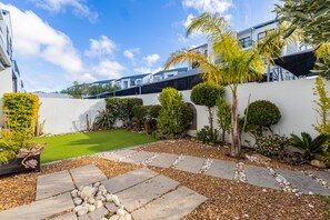 A landscaped garden with a lawn, stone pathway, and various plants. - Spacious 3BR Garden Pool Gym Parking by Ctha (Cape Town)