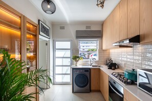 A modern kitchen with a built-in washer, a window with a view, and wooden cabinets. - Pet-friendly Studio With Private Patio and by Ctha (Cape Town)