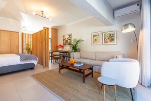 A modern living room with a sofa, a coffee table with books and fruit, a dining area with chairs, and a wooden partition. - Pet-friendly Studio With Private Patio and by Ctha (Cape Town)