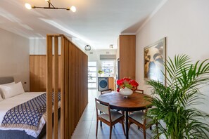 A modern bedroom with a wooden partition, a bed with a patterned blanket, a dining table with chairs, and a potted plant. - Pet-friendly Studio With Private Patio and by Ctha (Cape Town)