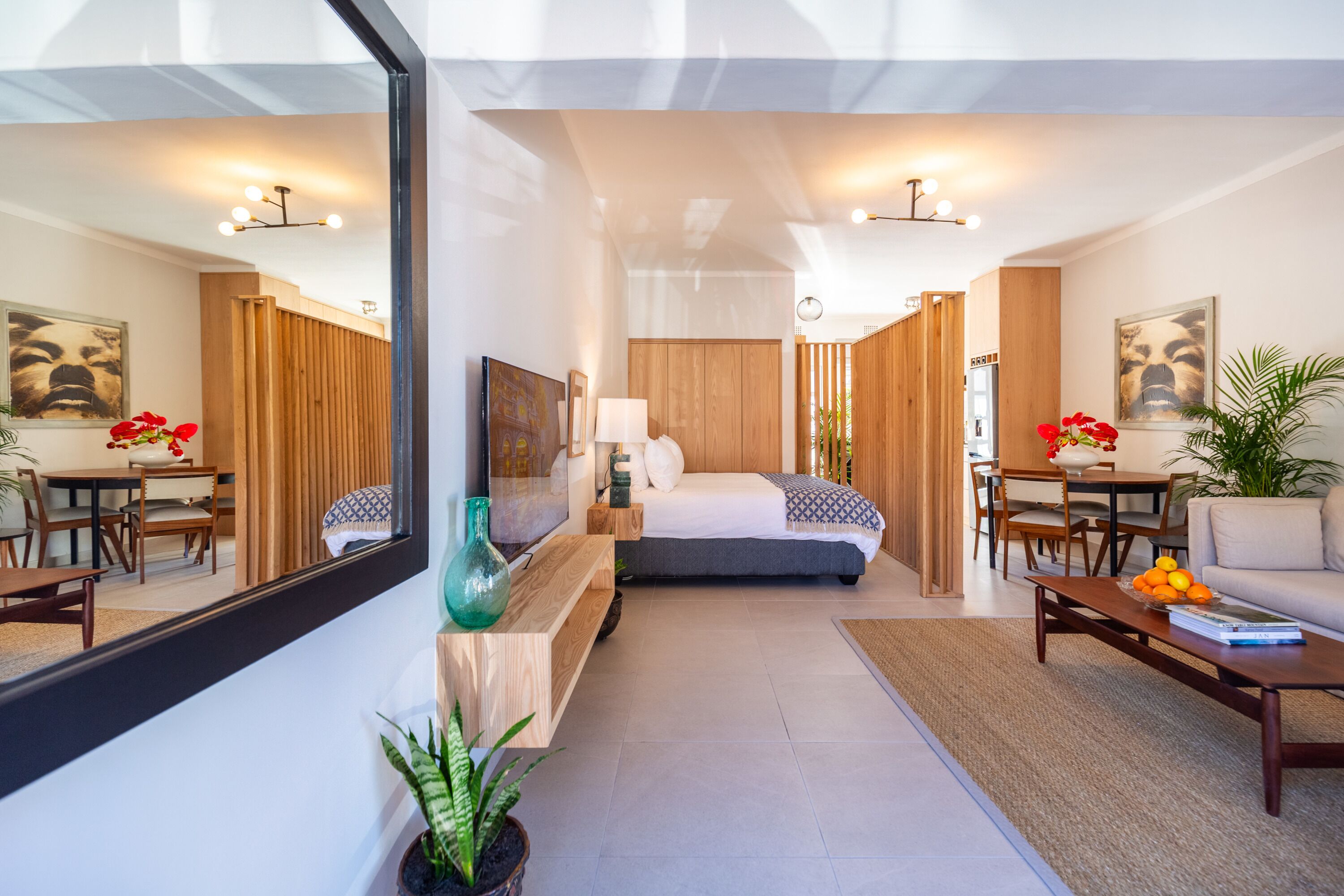 A modern hotel room with a large bed, a sitting area with a coffee table, a dining table, and a large mirror.