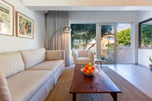 A modern living room with a sofa, a coffee table with fruit, and a view through a glass door to an outdoor area. - Pet-friendly Studio With Private Patio and by Ctha (Cape Town)