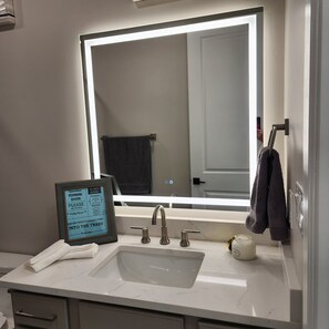 Un baño con un espejo grande, un lavabo y un cartel enmarcado sobre normas de fontanería.