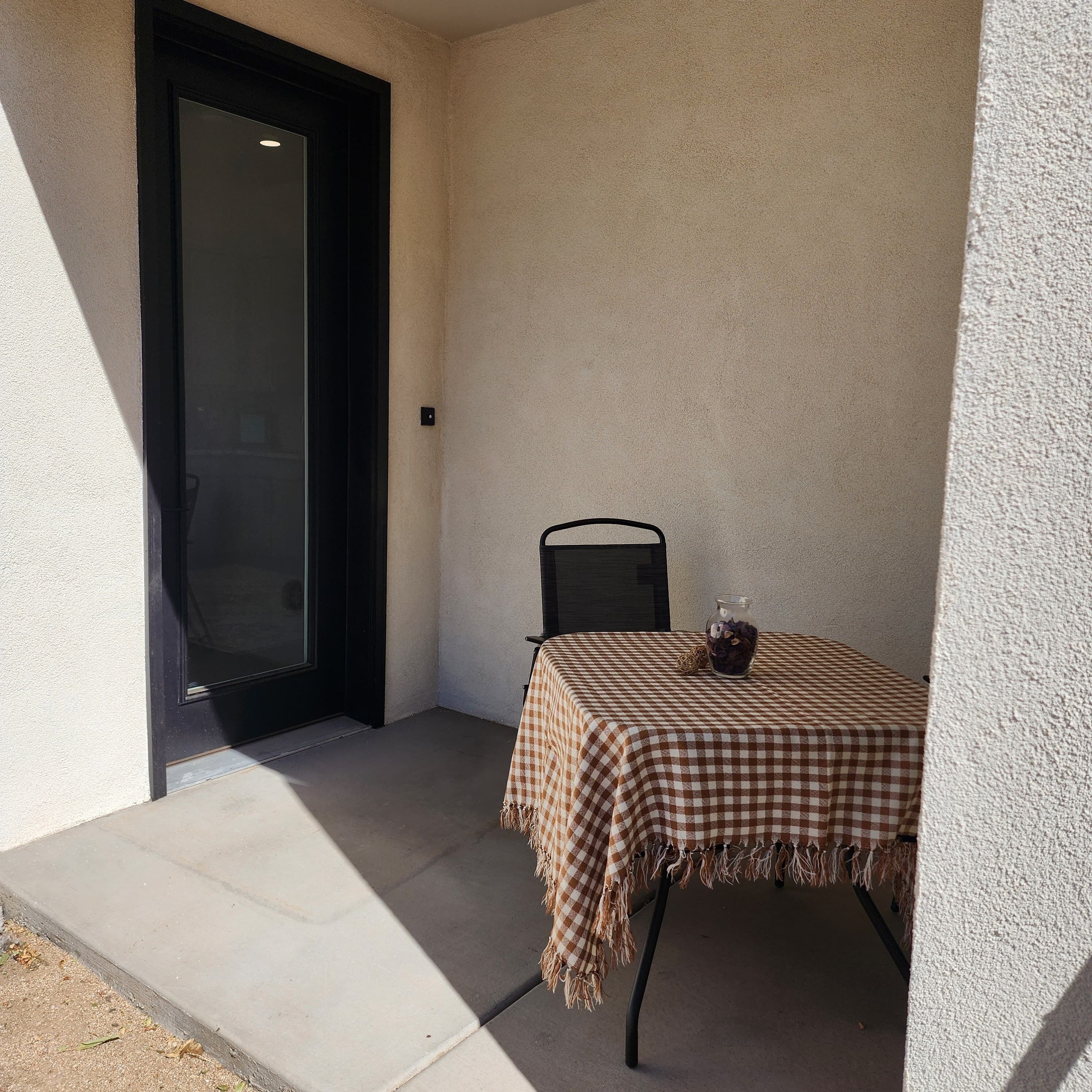 A small outdoor table with a checkered tablecloth, a chair, and a vase with dried flowers.