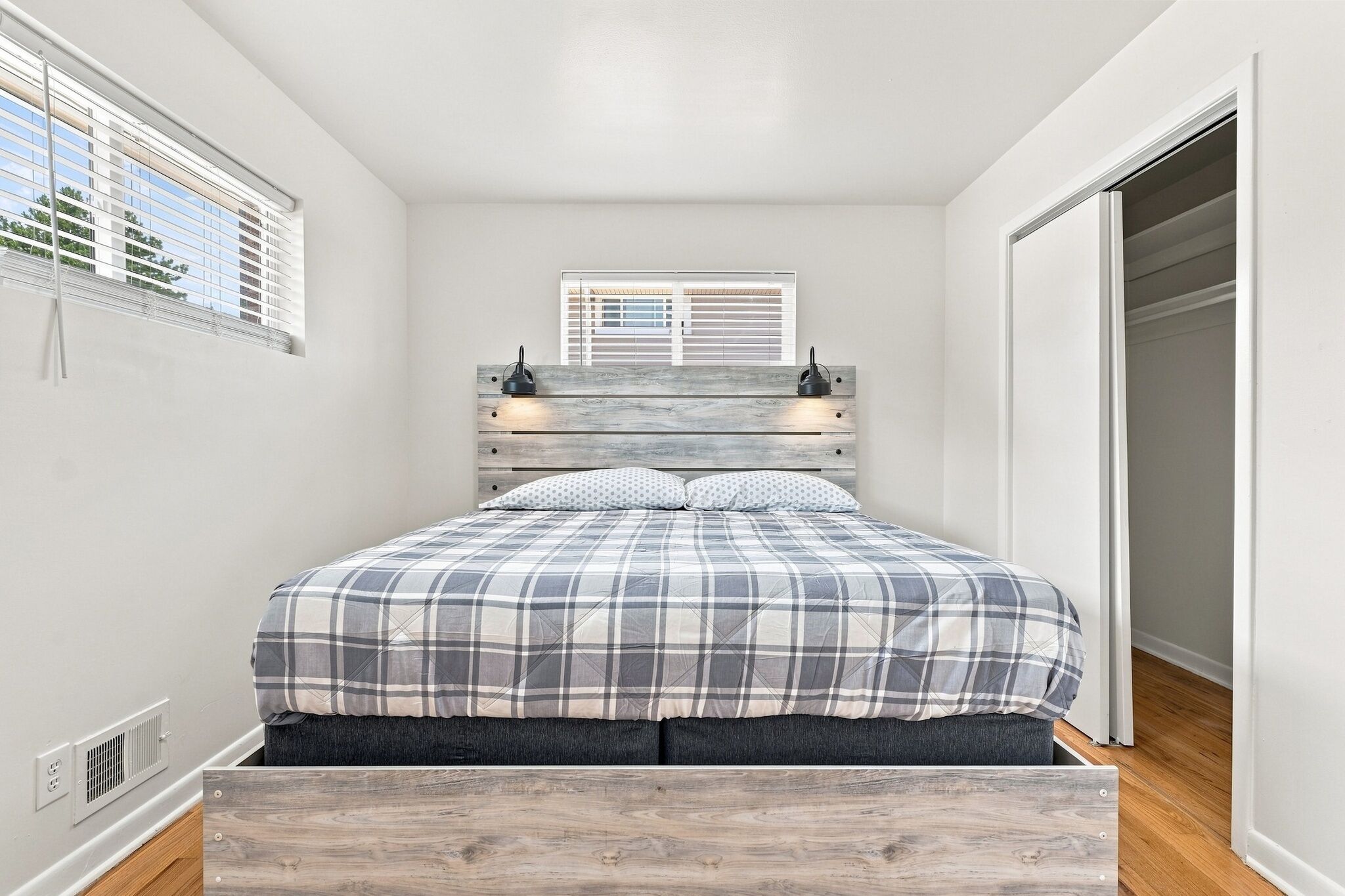 A bedroom with a bed, a window with blinds, a wardrobe, and a wall-mounted light fixture.