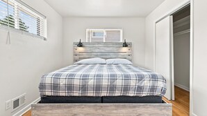 A bedroom with a bed, a window with blinds, a wardrobe, and a wall-mounted light fixture.