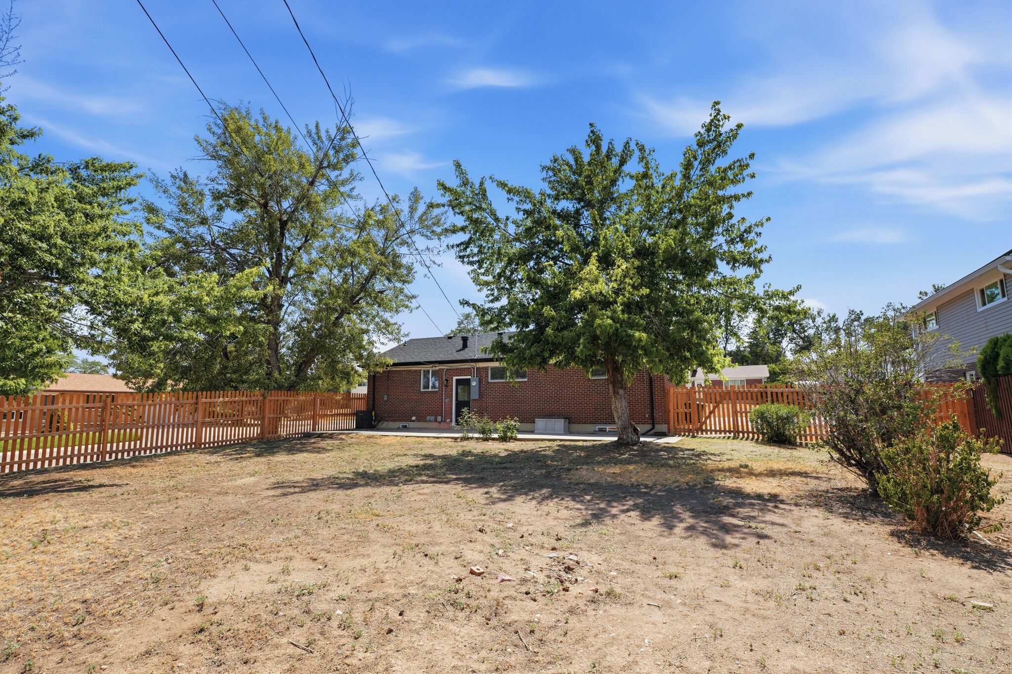 A residential property with a brick house, fenced yard, and mature trees.