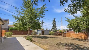 A residential backyard with a wooden fence, a small shed, and a concrete pathway.
