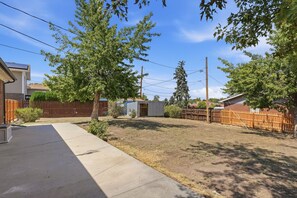 A residential backyard with a wooden fence, a small shed, and a concrete pathway.