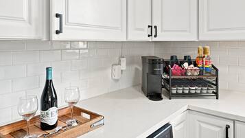A kitchen with white cabinets, a coffee maker, a wine bottle, and a tray with glasses.