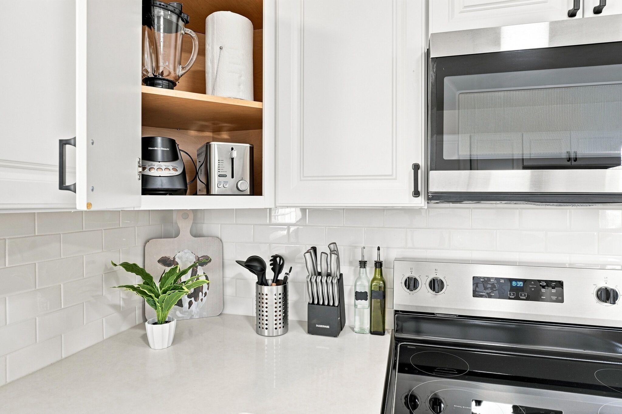 A kitchen with white cabinets, a stainless steel oven, a microwave, and various kitchen utensils.