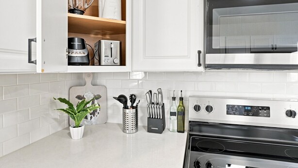 A kitchen with white cabinets, a stainless steel oven, a microwave, and various kitchen utensils.