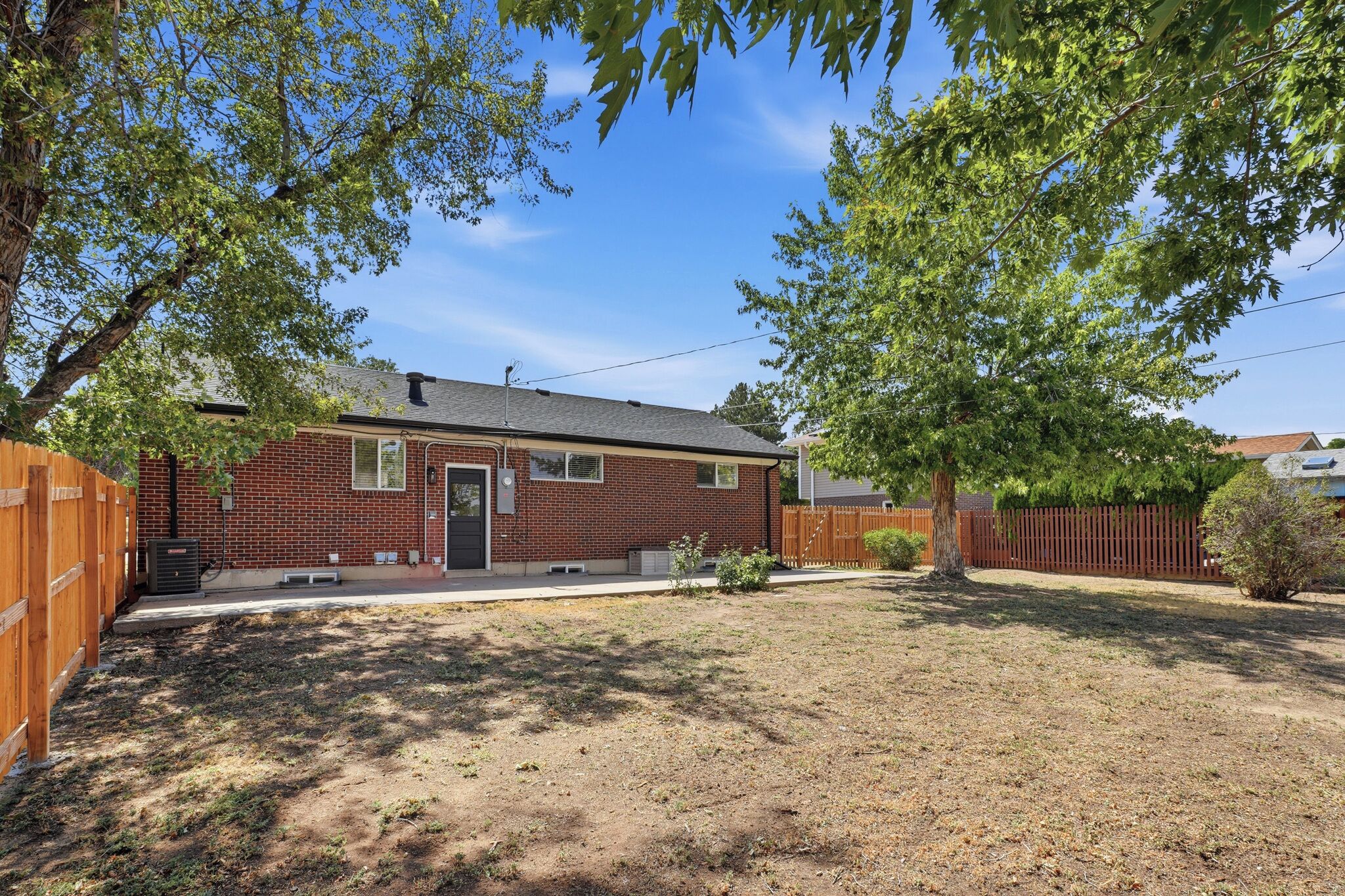 A single-story brick house with a front yard, a wooden fence, and a tree providing shade.