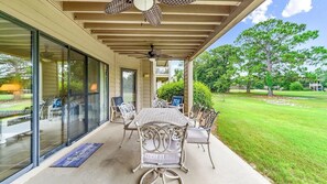 Eine Außenveranda mit Tisch und Stühlen, einem Deckenventilator und Blick auf einen gepflegten Rasen und Bäume.
