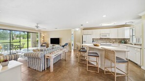 A spacious living area with a large window, a sofa set, a dining area with bar stools, and a kitchen with white cabinets. - Coucher du Soleil at Seascape, 3 bedroom Condo Miramar Beach Florida (Miramar Beach)