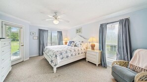 Ein Schlafzimmer mit Bett, Nachttischen, einem Sessel, einem Deckenventilator und einem Fenster mit Vorhängen.