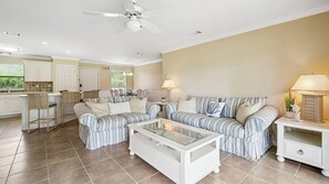 A living room with a striped sofa set, a glass coffee table, and a ceiling fan. - Coucher du Soleil at Seascape, 3 bedroom Condo Miramar Beach Florida (Miramar Beach)