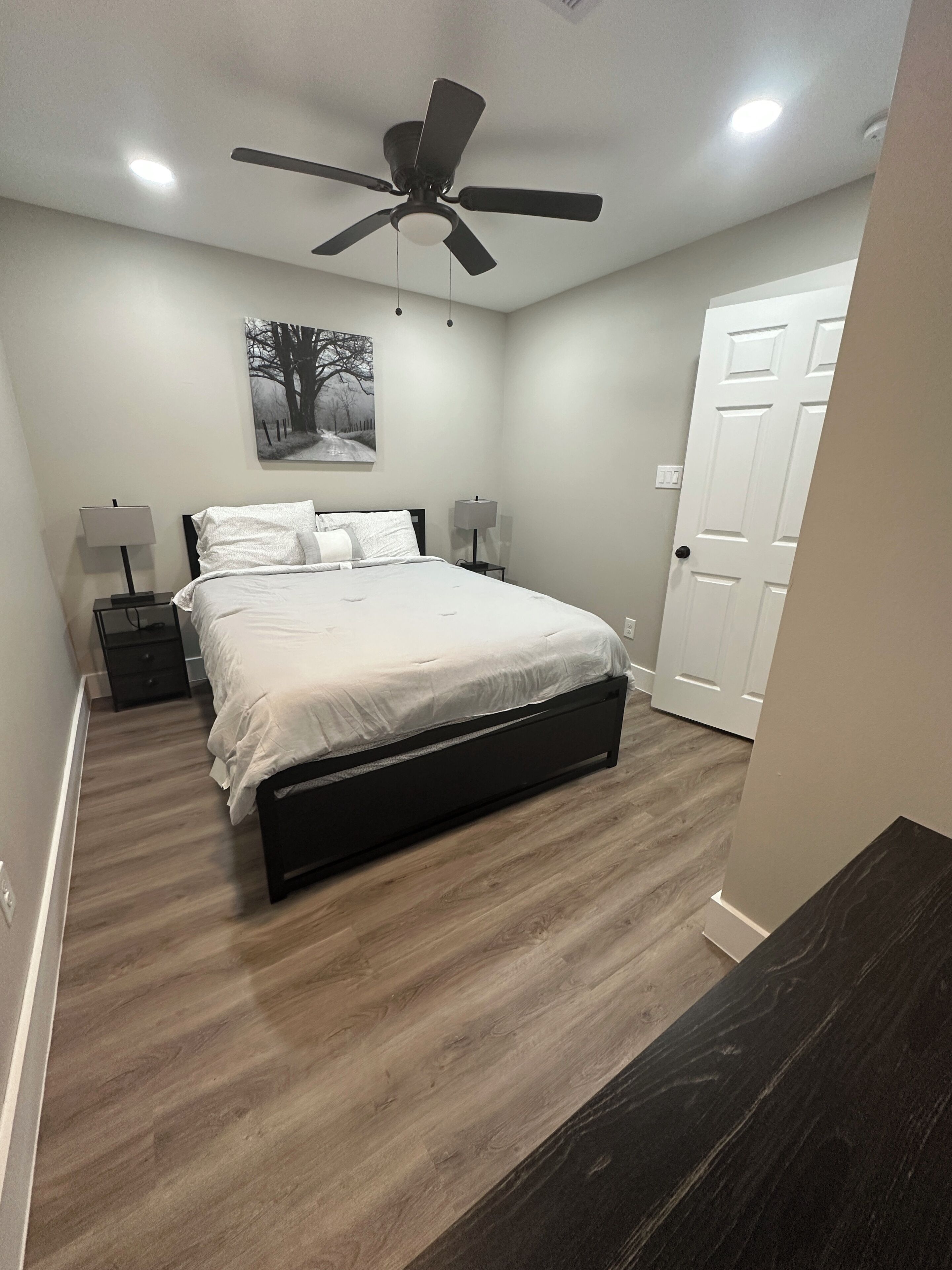 A bedroom with a bed, nightstands, a ceiling fan, and a door.