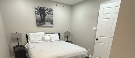 Une chambre à coucher avec un lit, des tables de chevet, un ventilateur de plafond et une porte.