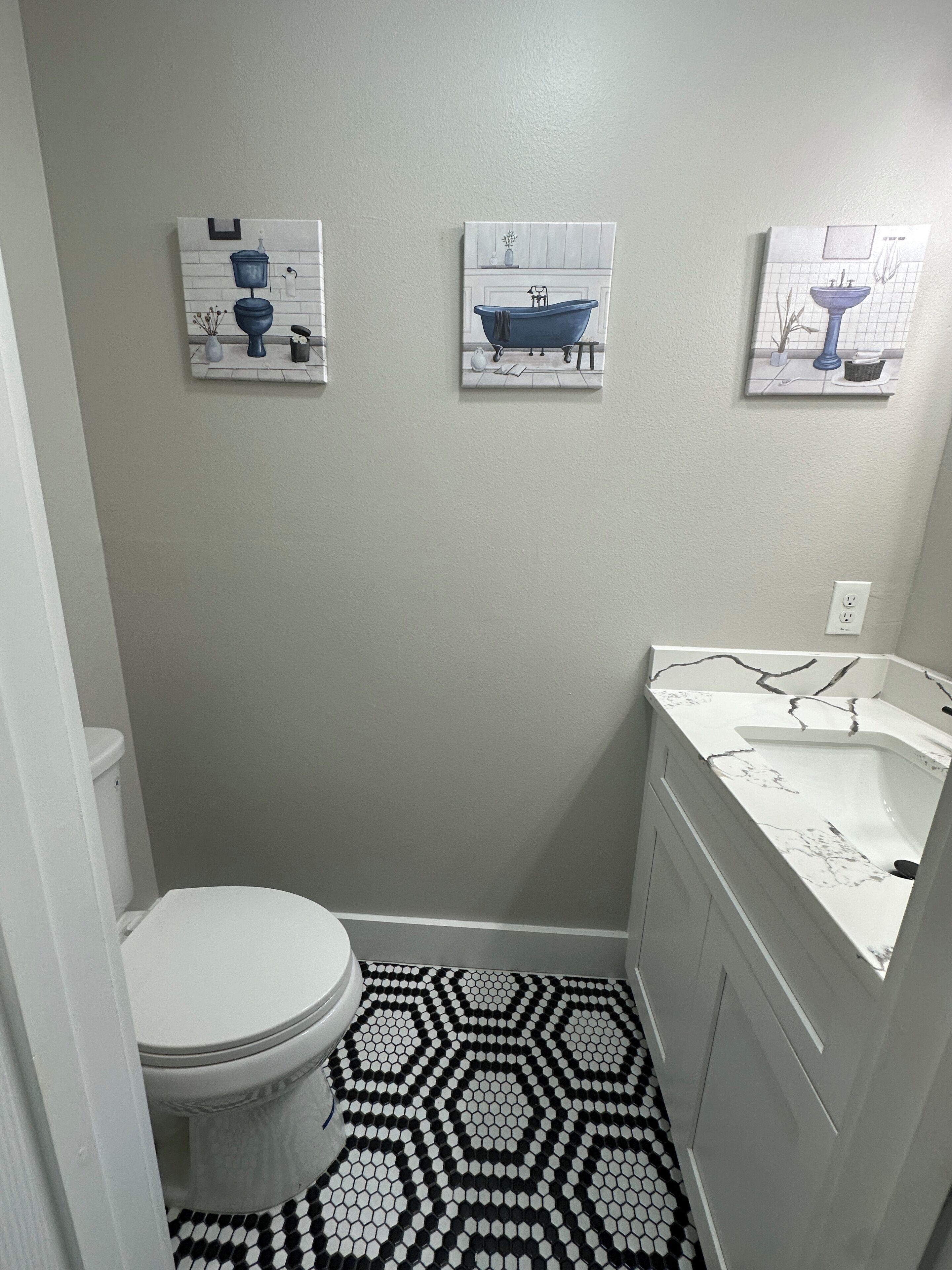 A small bathroom with a toilet, a sink, and three wall-mounted artwork pieces.