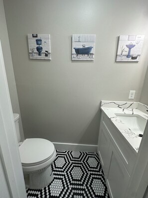 Un baño pequeño con inodoro, lavamanos y tres obras de arte colgadas en la pared.