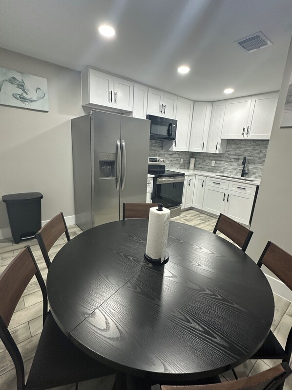 Una cocina moderna con armarios blancos, electrodomésticos de acero inoxidable y una mesa redonda con sillas.
