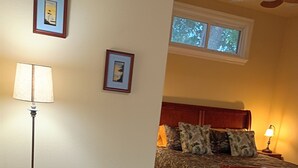 A room with a bed, a desk, a chair, a lamp, a ceiling fan, and a window. - Private Woodland Cottage—Secluded Yet 5 Minutes from Town (Poplarville)
