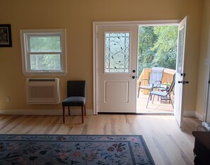 A room with a door leading to an outdoor area, a window, a chair, and a patterned rug.