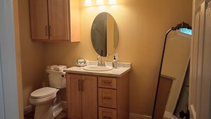 A bathroom with a toilet, sink, vanity, mirror, and a shower area. - Private Woodland Cottage—Secluded Yet 5 Minutes from Town (Poplarville)